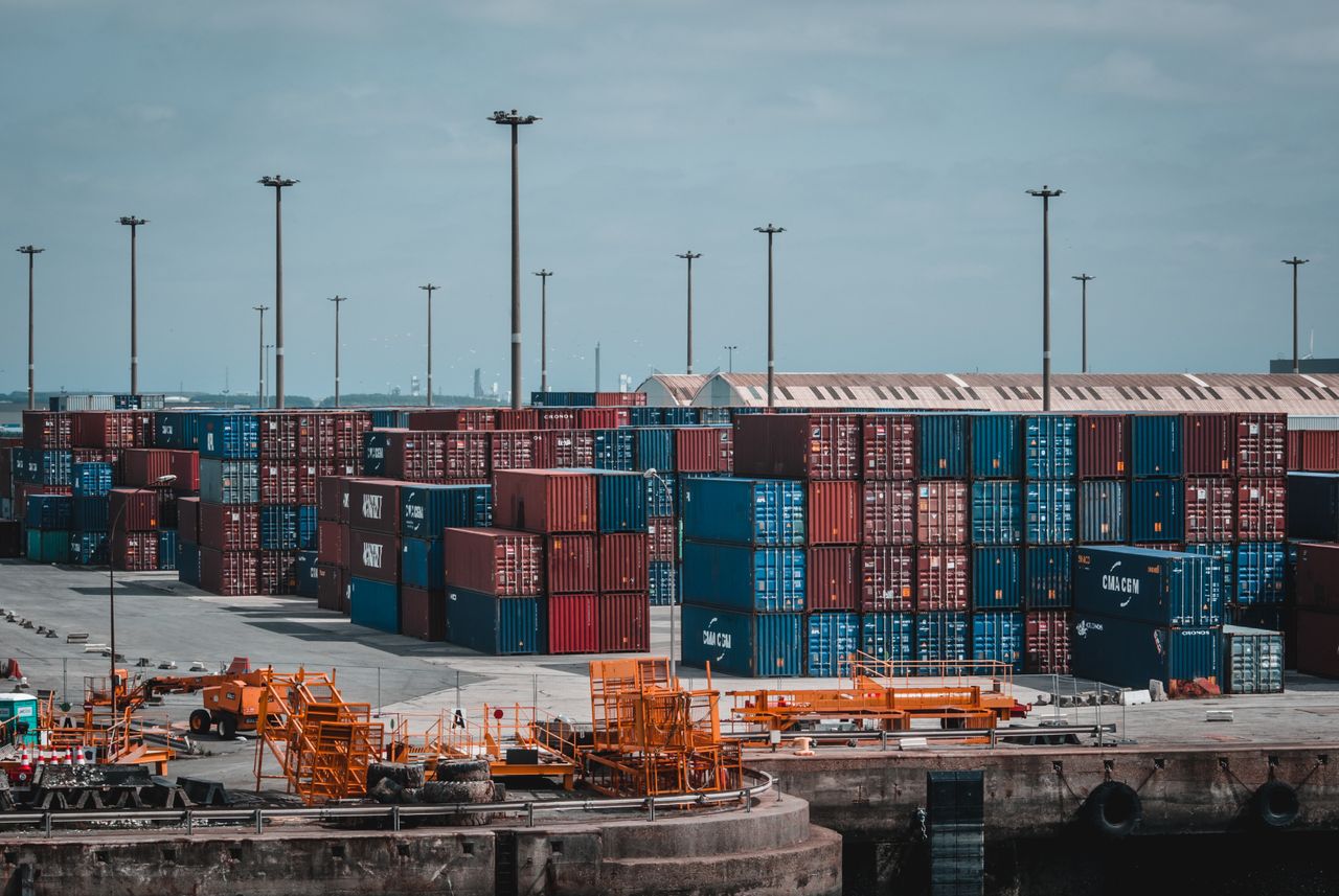 Row of vibrant cargo containers on train tracks under a clear blue sky.