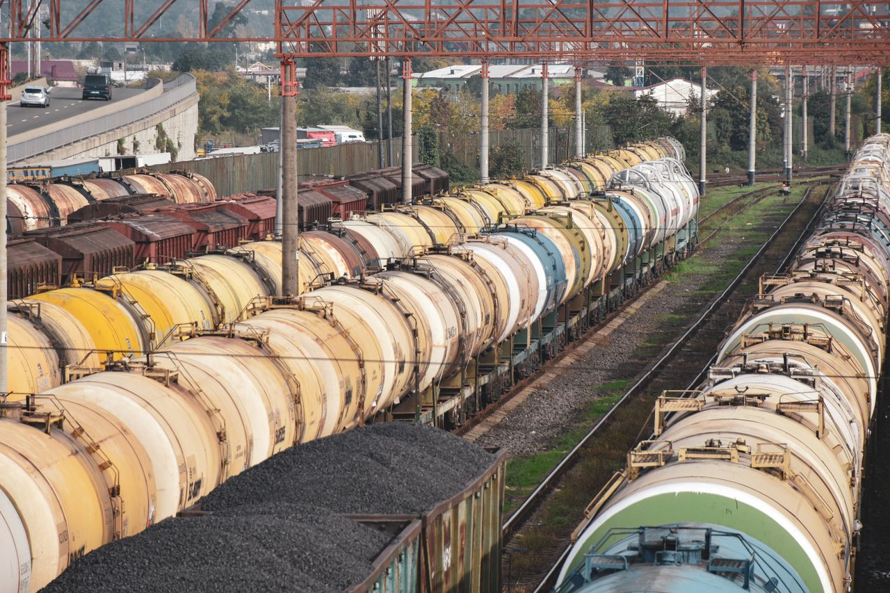 A long freight train with colorful tank cars on a railway track under a bright sky.
