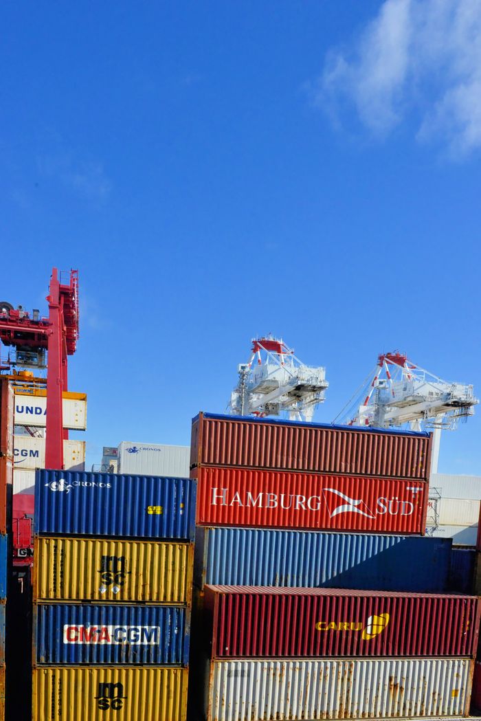 Large red cargo ship transporting goods across the ocean under a bright blue sky.