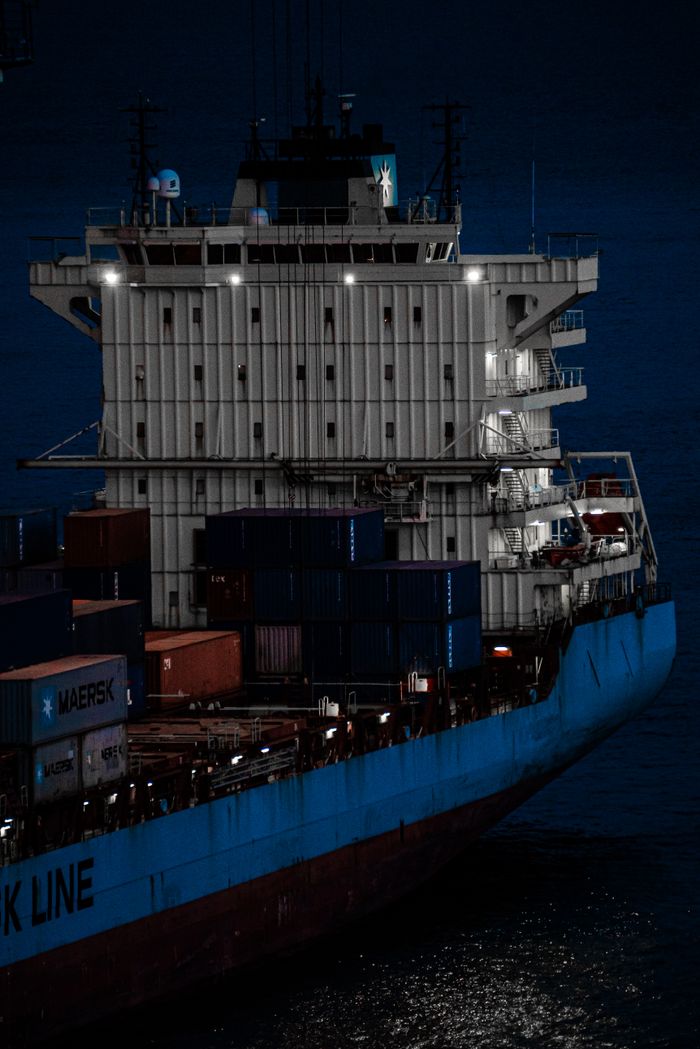 Aerial view of a cargo ship carrying containers and colorful vehicles on the open sea.