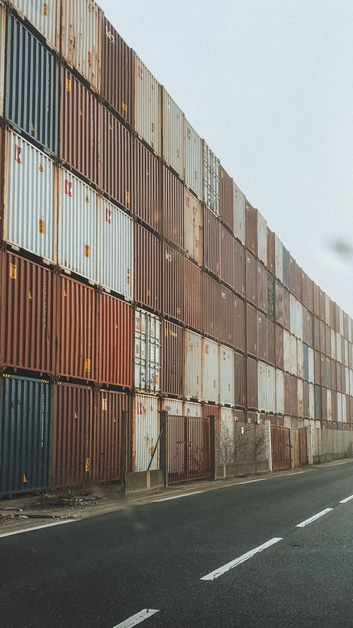 High-rise stack of shipping containers along an industrial road in foggy weather.
